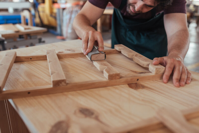 Craftsman showing how to sand wood in his workshop