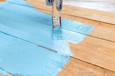 painting raw wood with blue-colored paint and a paintbrush